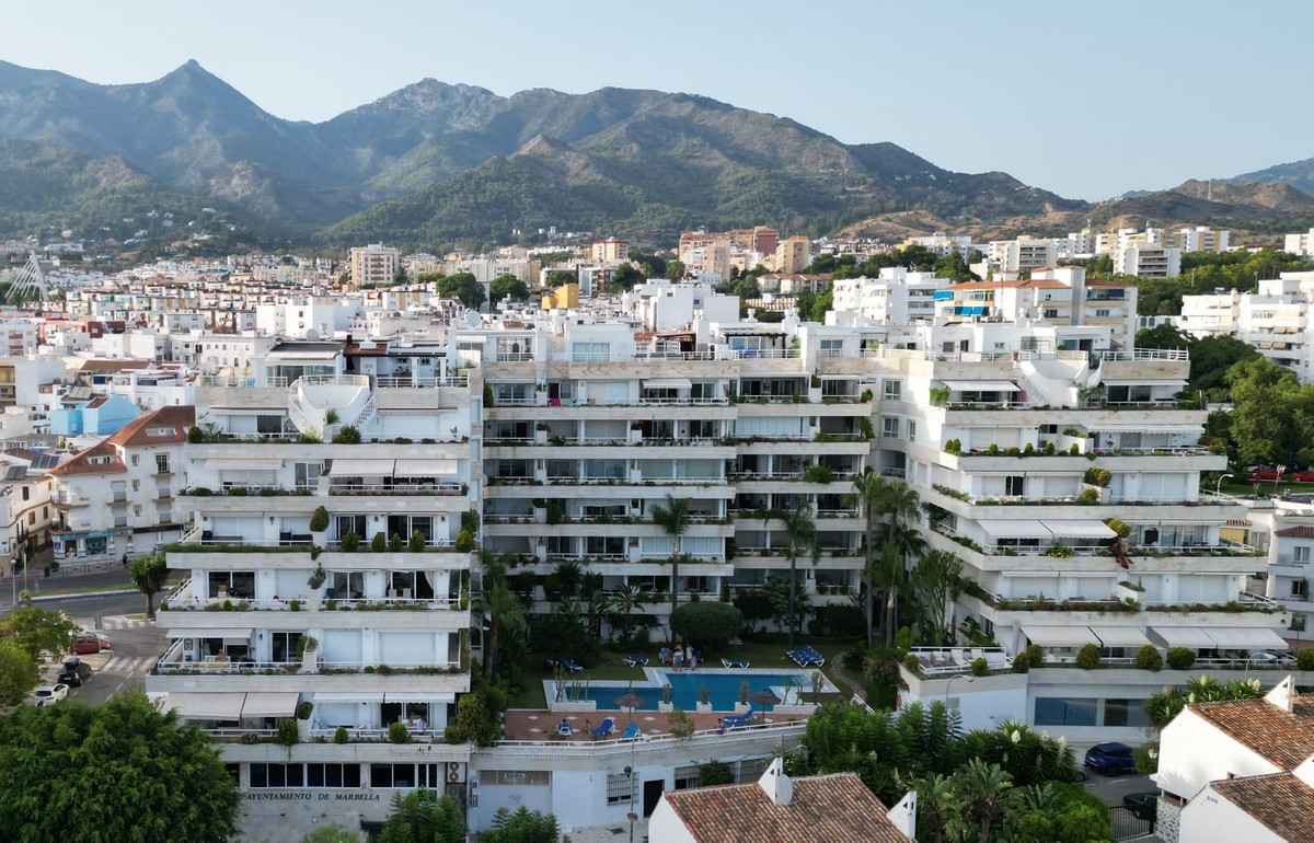 Overzicht van een appartementencomplex in Marbella met zwembad en bergen op de achtergrond.
