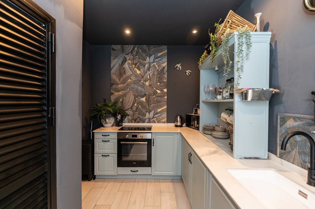 Modern kitchen featuring light blue cabinets, a botanical wallpaper accent wall, integrated oven, and a large sink with a black faucet.