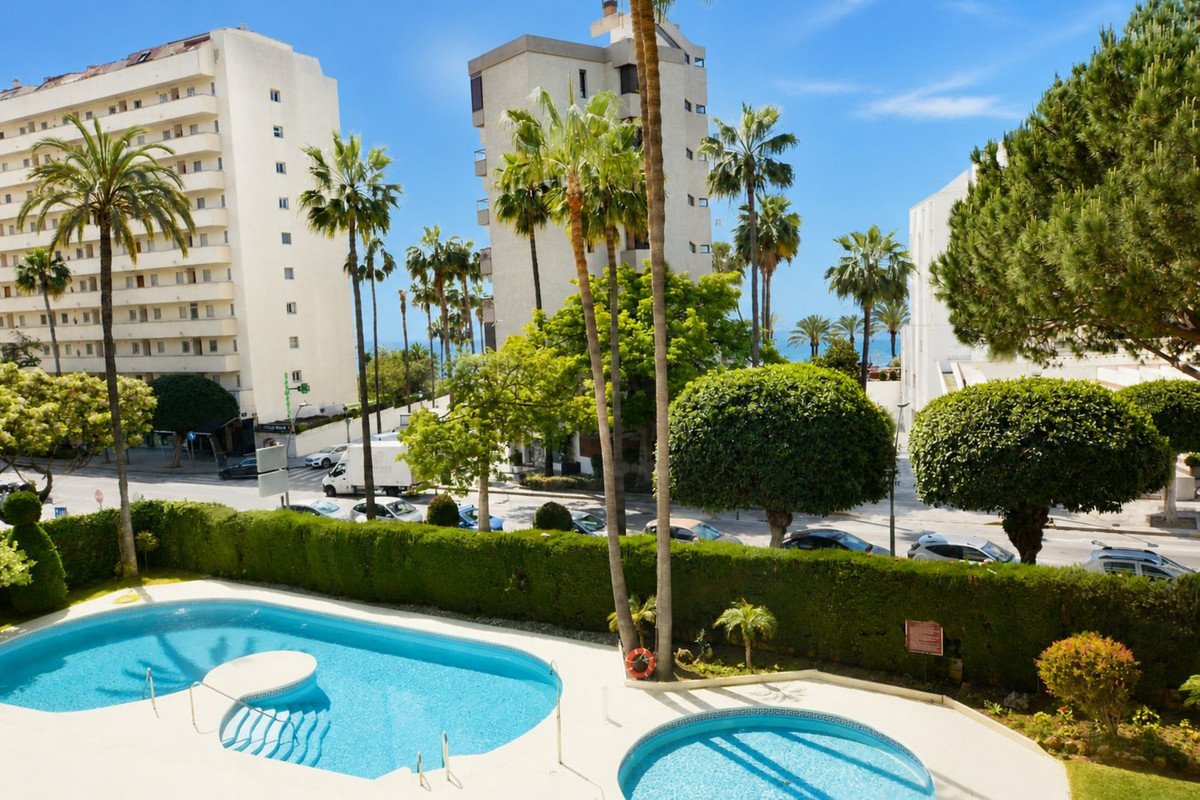 Apartment with pool view, palm trees, and ocean in background.