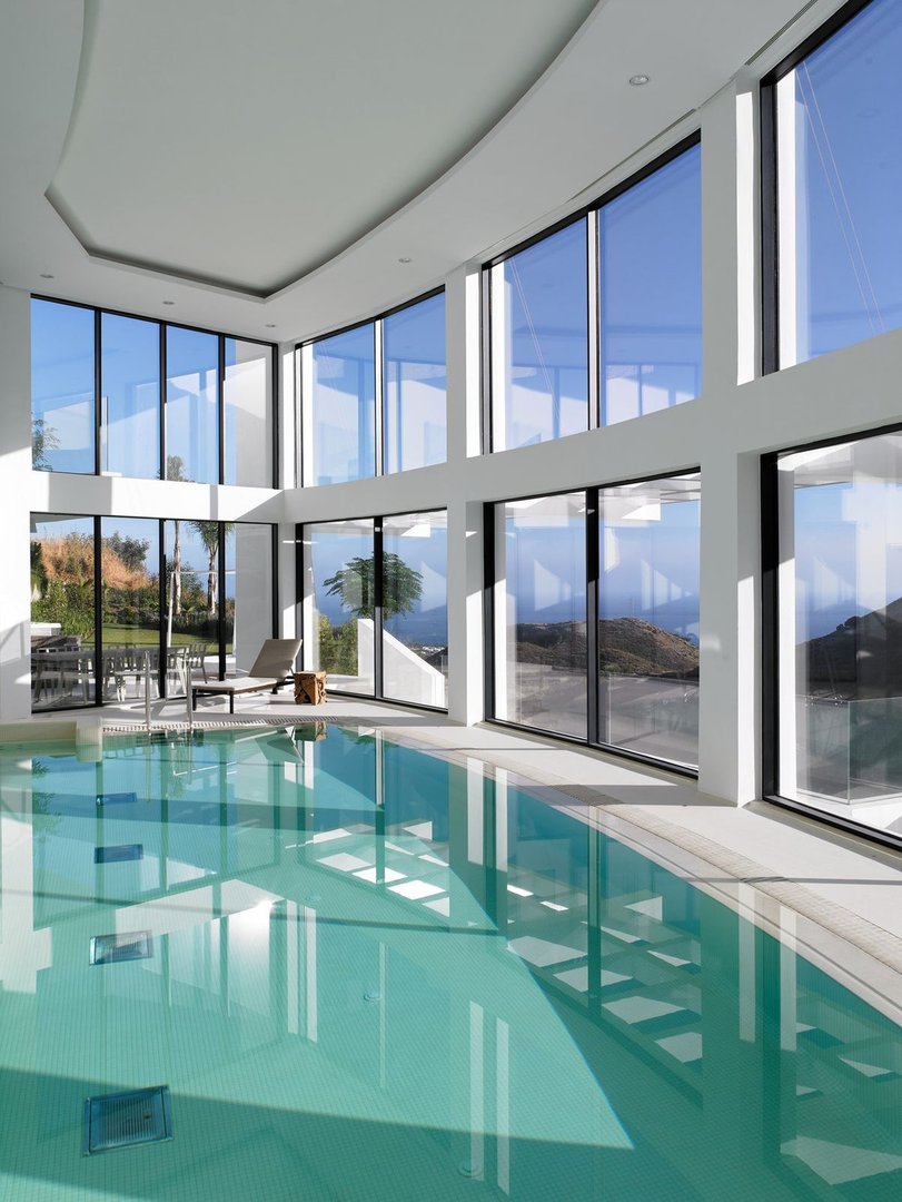 Indoor swimming pool with panoramic windows overlooking mountains and greenery