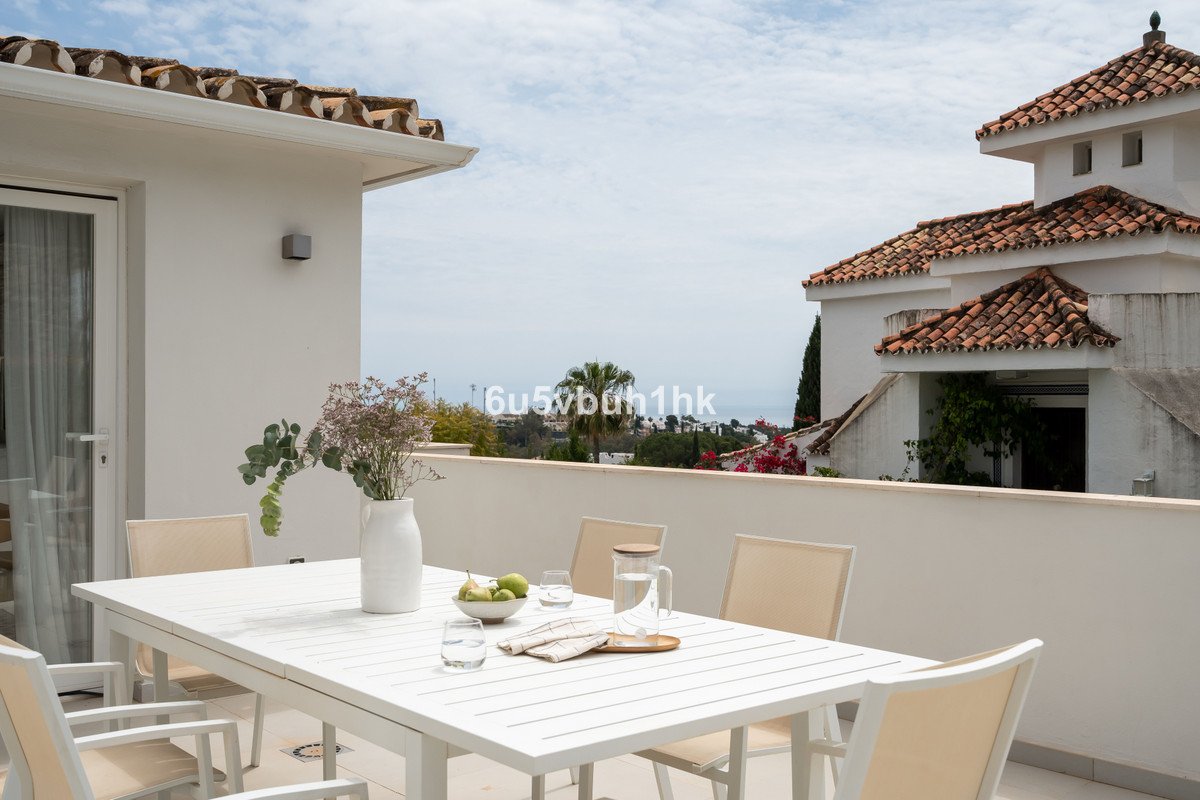 Terrace with dining table and chairs, overlooking a distant sea view and Mediterranean architecture.