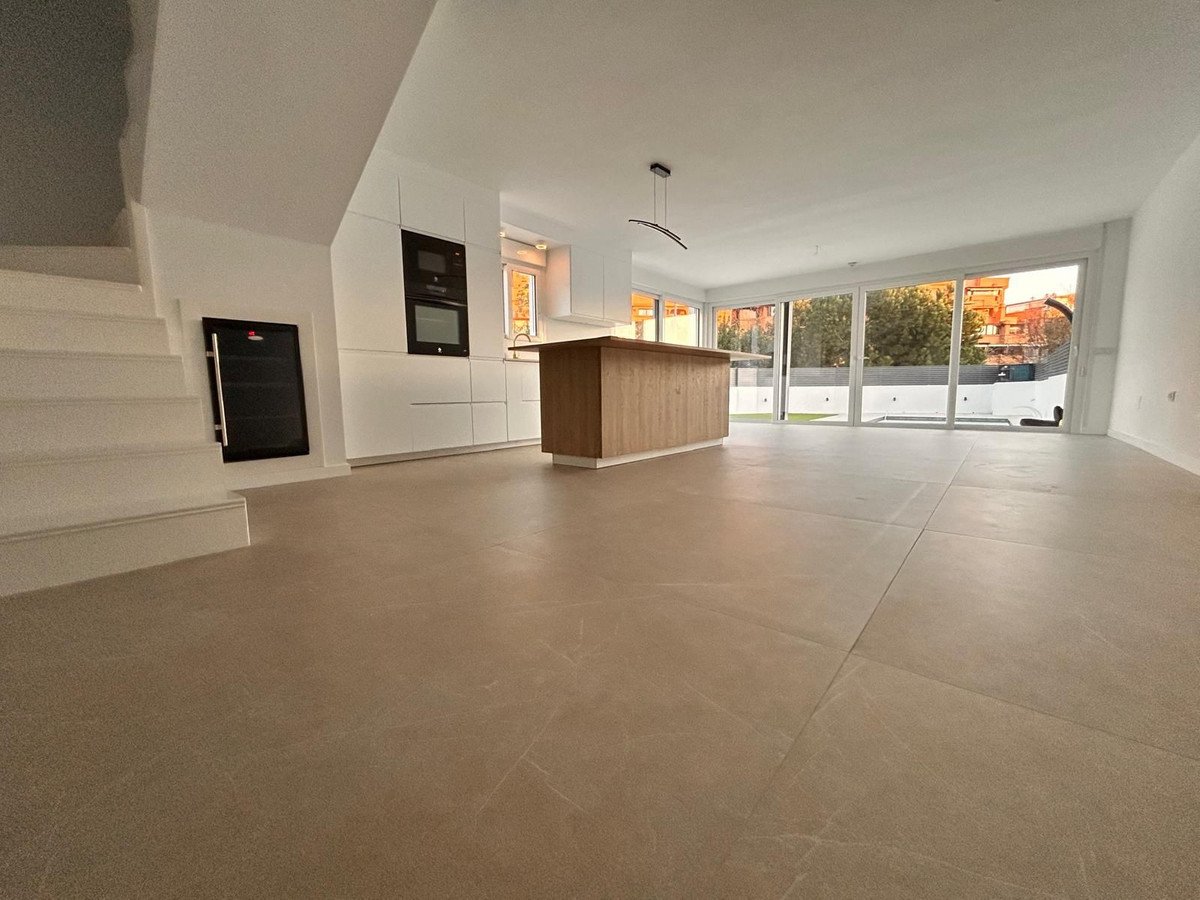 Modern open-plan living area and kitchen with a central island and large glass doors leading to an outdoor space.