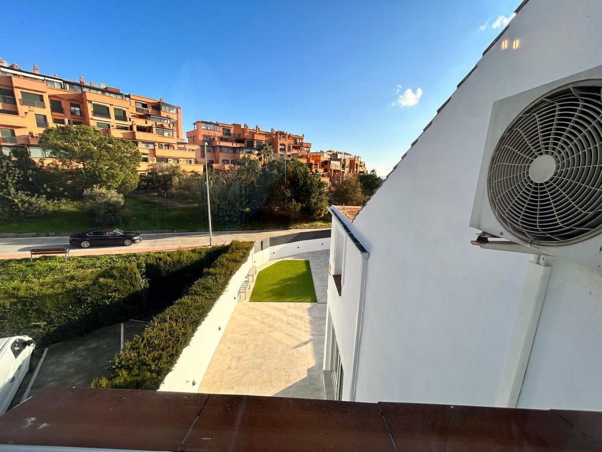 View from a balcony overlooking a courtyard with artificial grass, a paved area, and apartment buildings in the background.