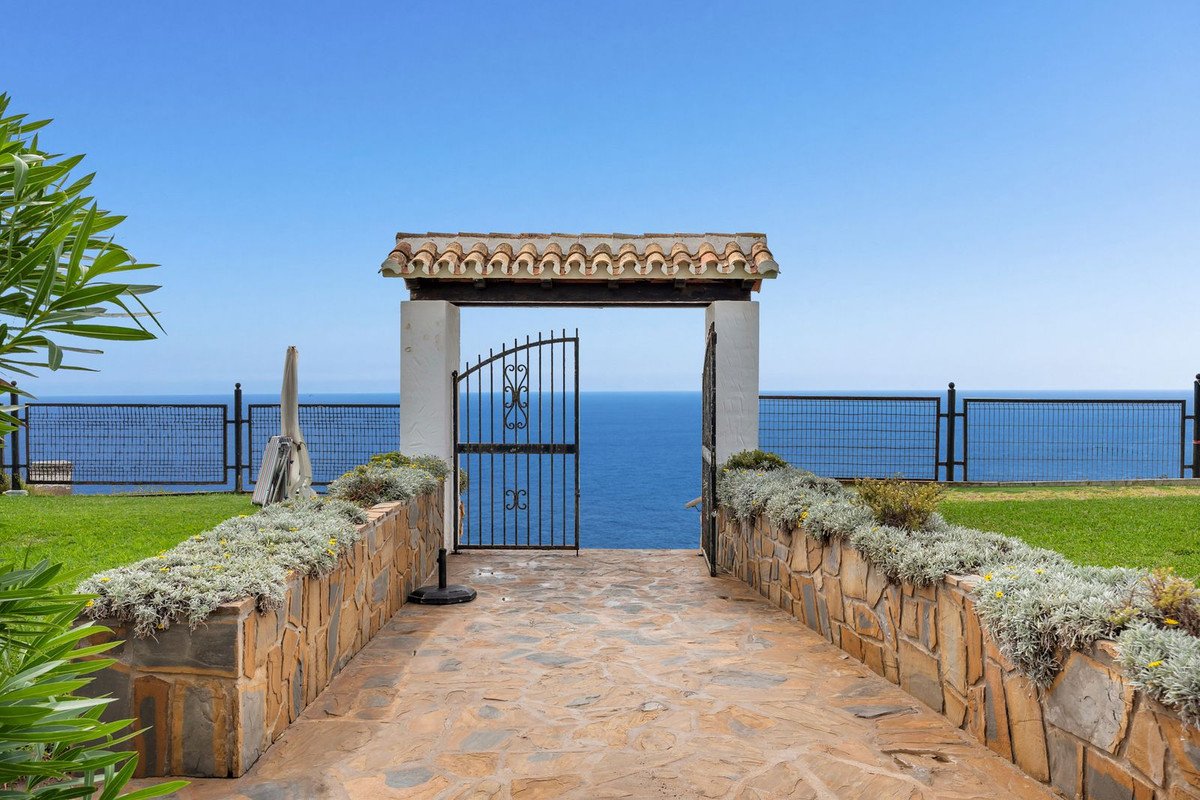 Gated stone pathway leading to ocean view with tiled arch and metal fencing