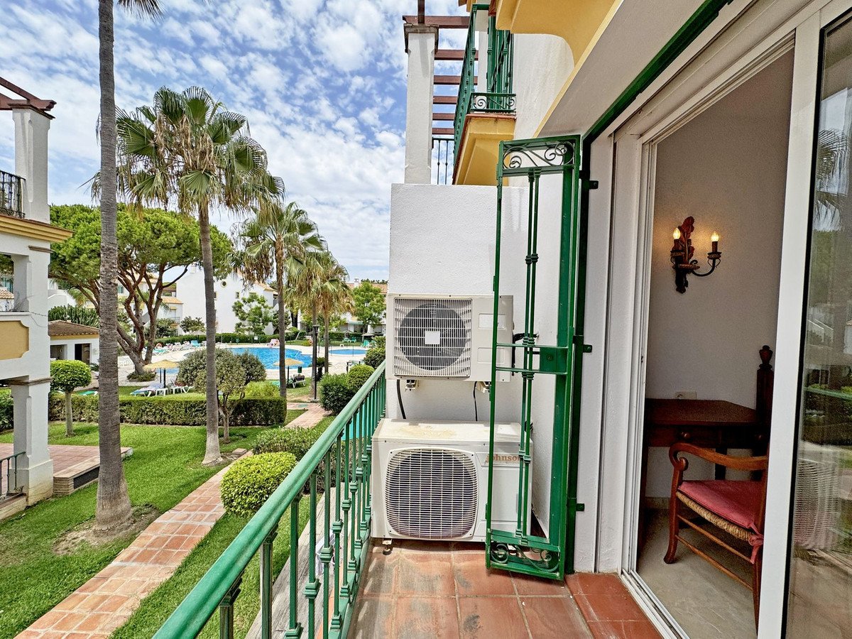 View from the balcony showing a swimming pool, palm trees, and garden area. Air conditioning units are visible.