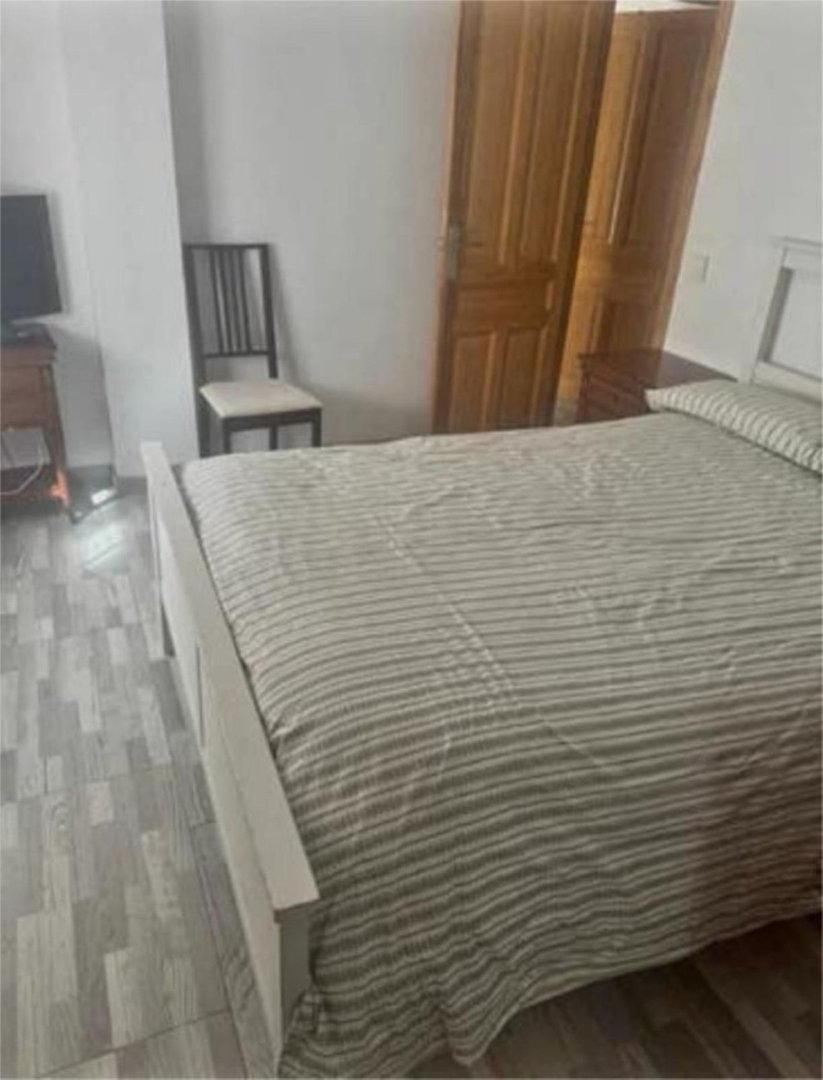 A bedroom with a bed, striped bedding, a chair, wooden doors, and a television in the background.