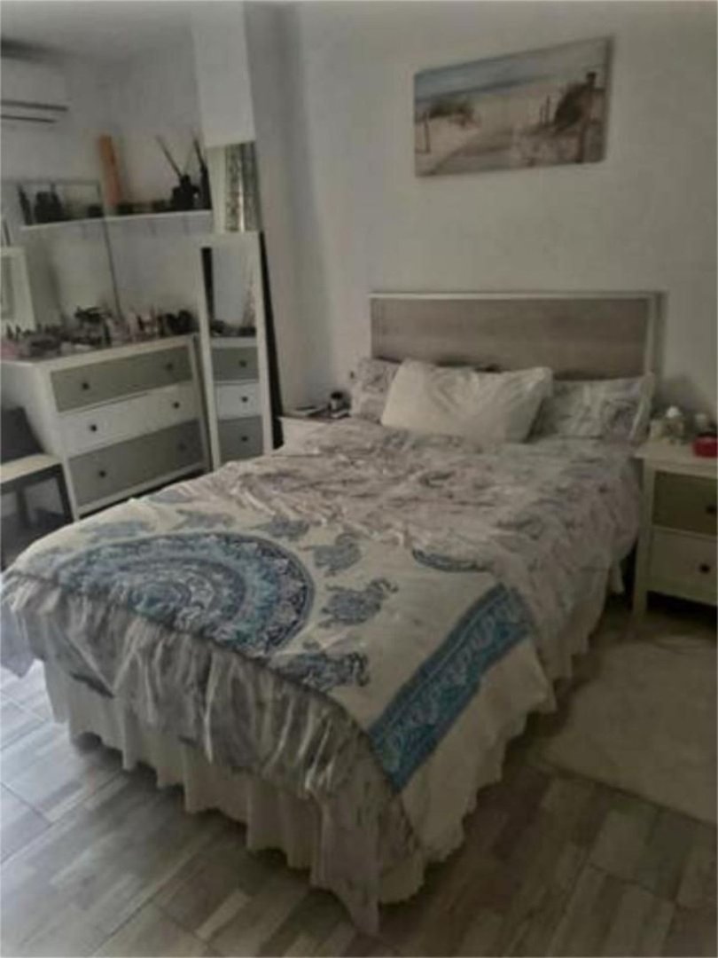 A bedroom featuring a queen-size bed with patterned bedding, a dresser, and a decorative wall painting.