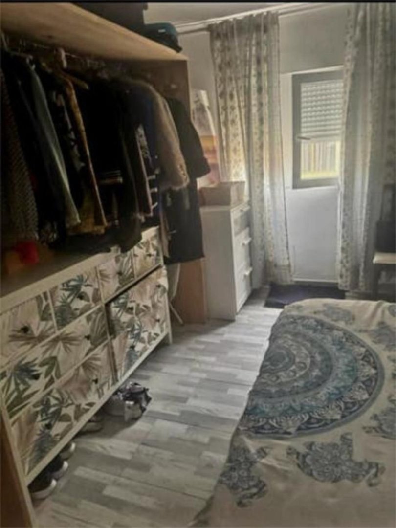 A bedroom with an open closet, decorative dresser, and a window with blinds and curtains.