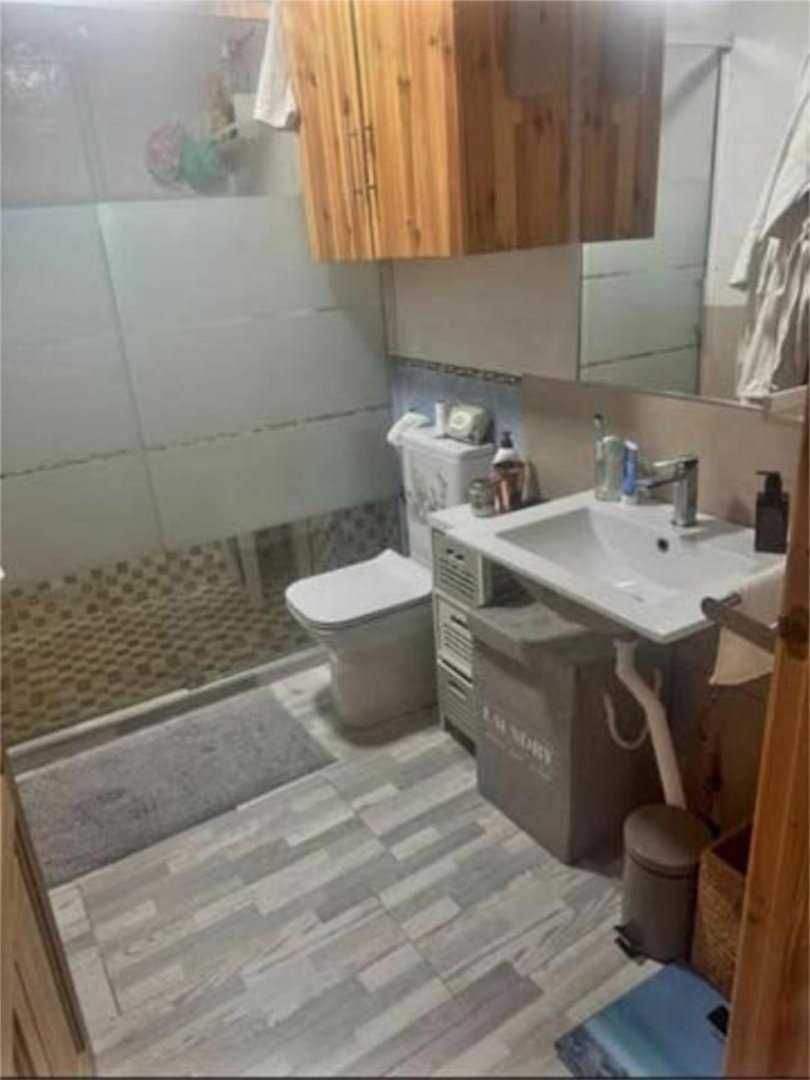 A compact modern bathroom with a sink, toilet, and wooden cabinetry above.