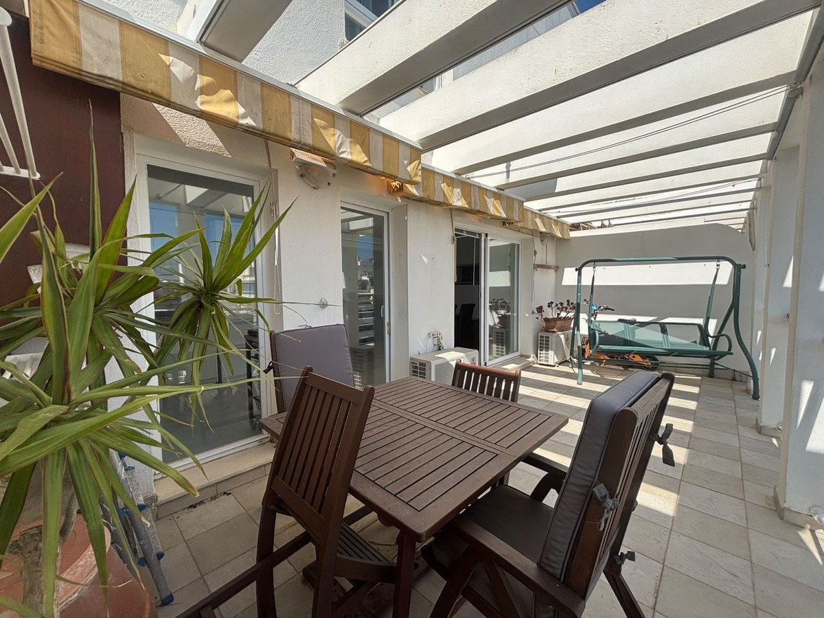 A covered balcony with a dining table, chairs, a swing set, and an air conditioning unit.