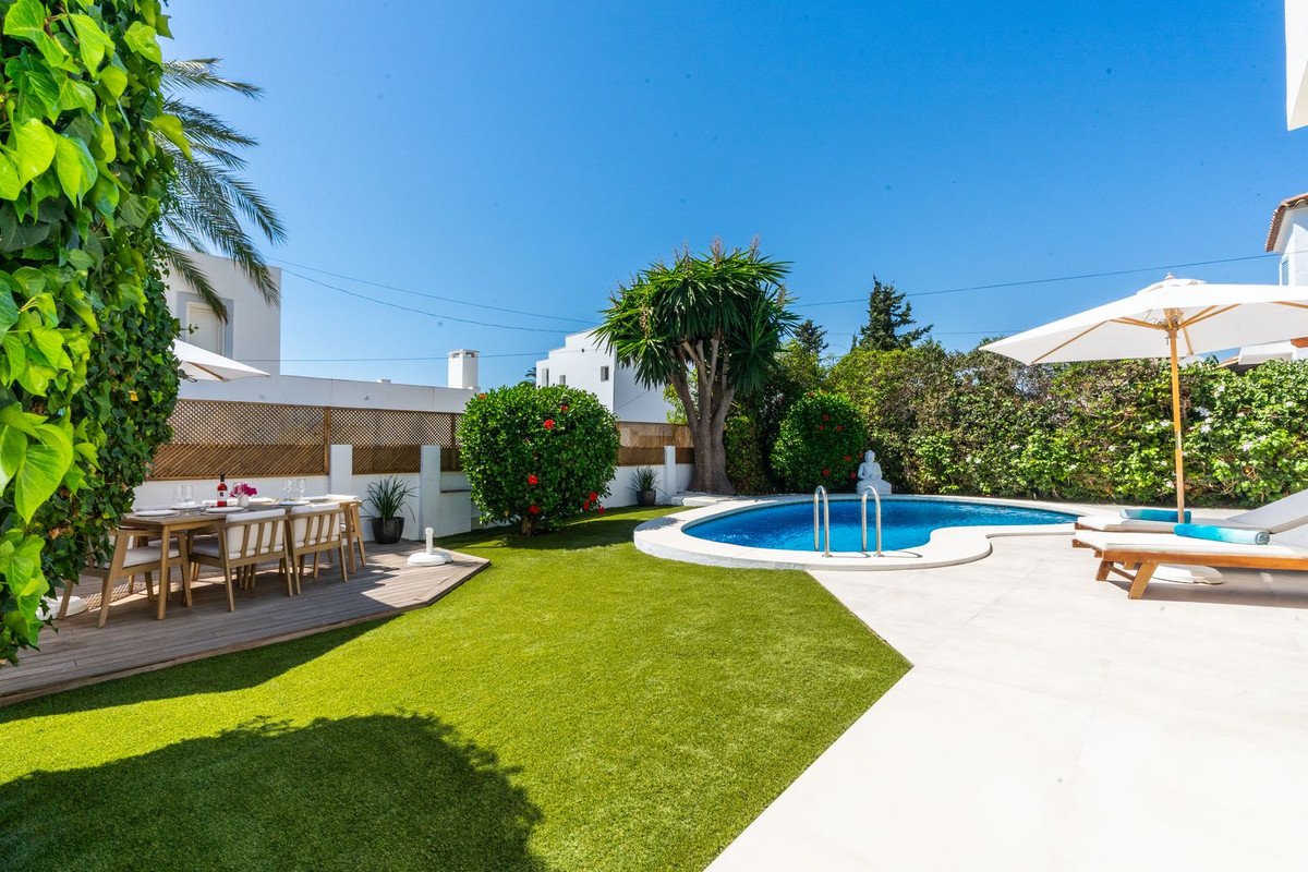 Outdoor dining area with a pool, lounge chairs, and a large umbrella under a clear blue sky.