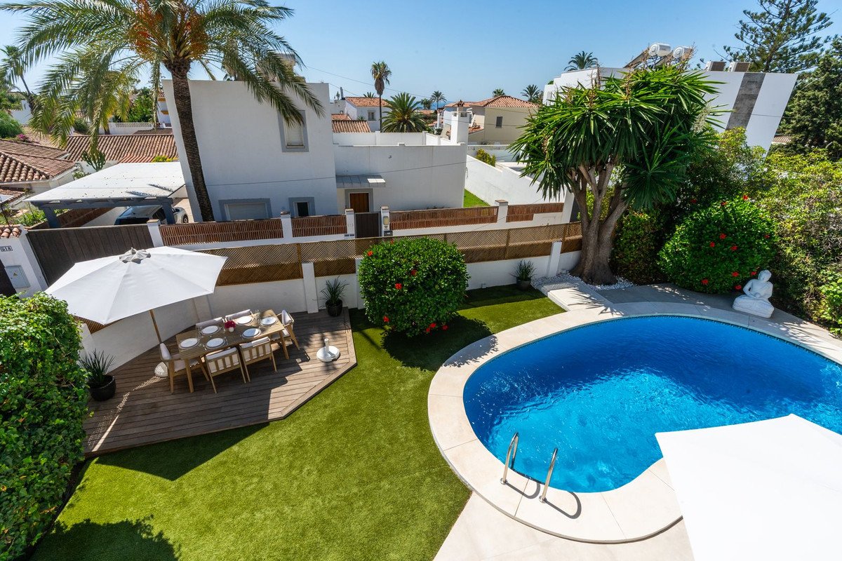 A beautiful outdoor space with a swimming pool, dining area with umbrella, and lush green lawn.