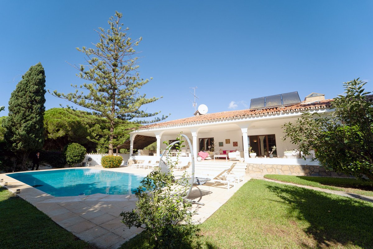 Villa with swimming pool, patio, and lush garden under clear blue sky