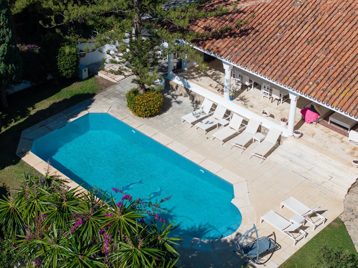 Aerial view of a backyard with a swimming pool and lounge chairs near a covered patio.