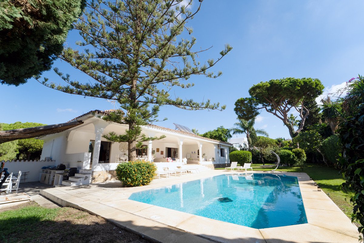 White villa with swimming pool, outdoor seating, and lush garden under clear blue sky