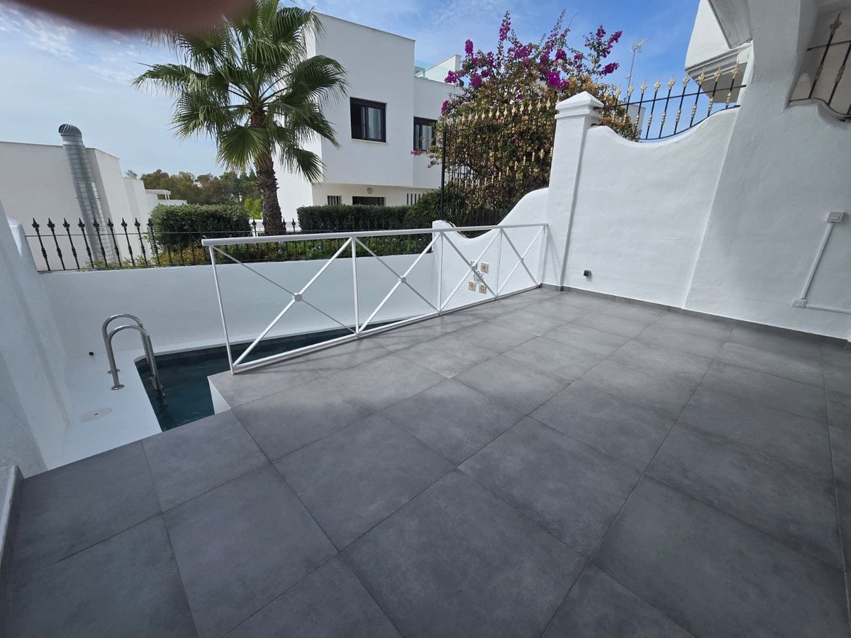 Spacious tiled terrace with a small pool and a palm tree overlooking a white building and blue sky.