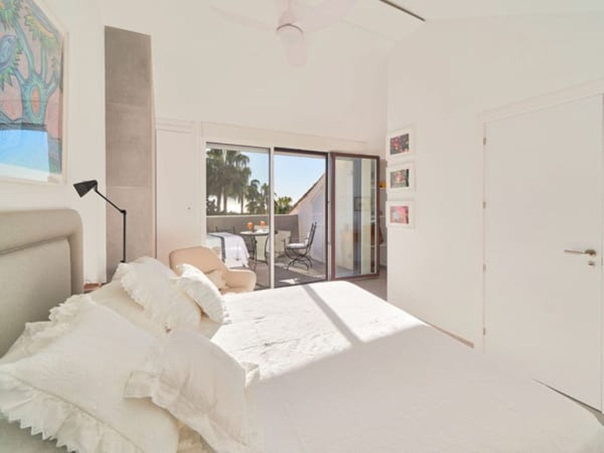 Bright master bedroom with white bedding and sliding glass doors to a balcony with outdoor seating