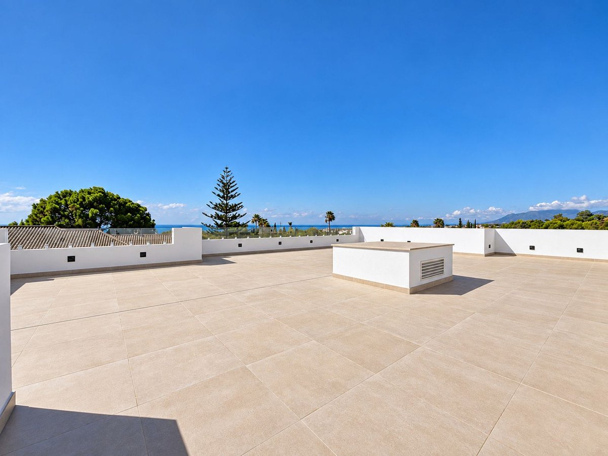 Spacious rooftop terrace with a sea view, featuring modern white railings and a built-in unit under a clear blue sky.