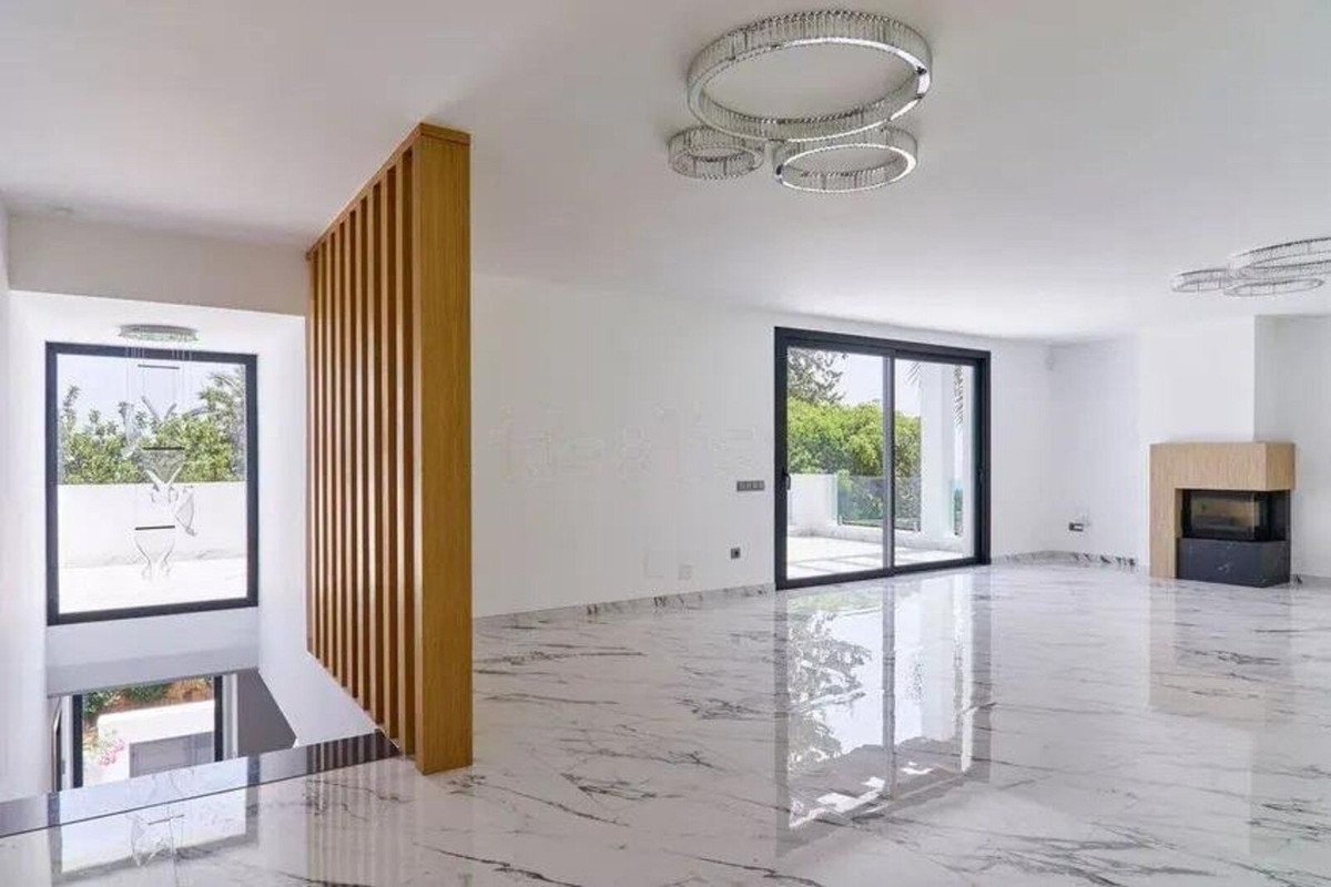 Modern living room with white marble floors, a contemporary fireplace, and large sliding glass doors offering an outdoor view.