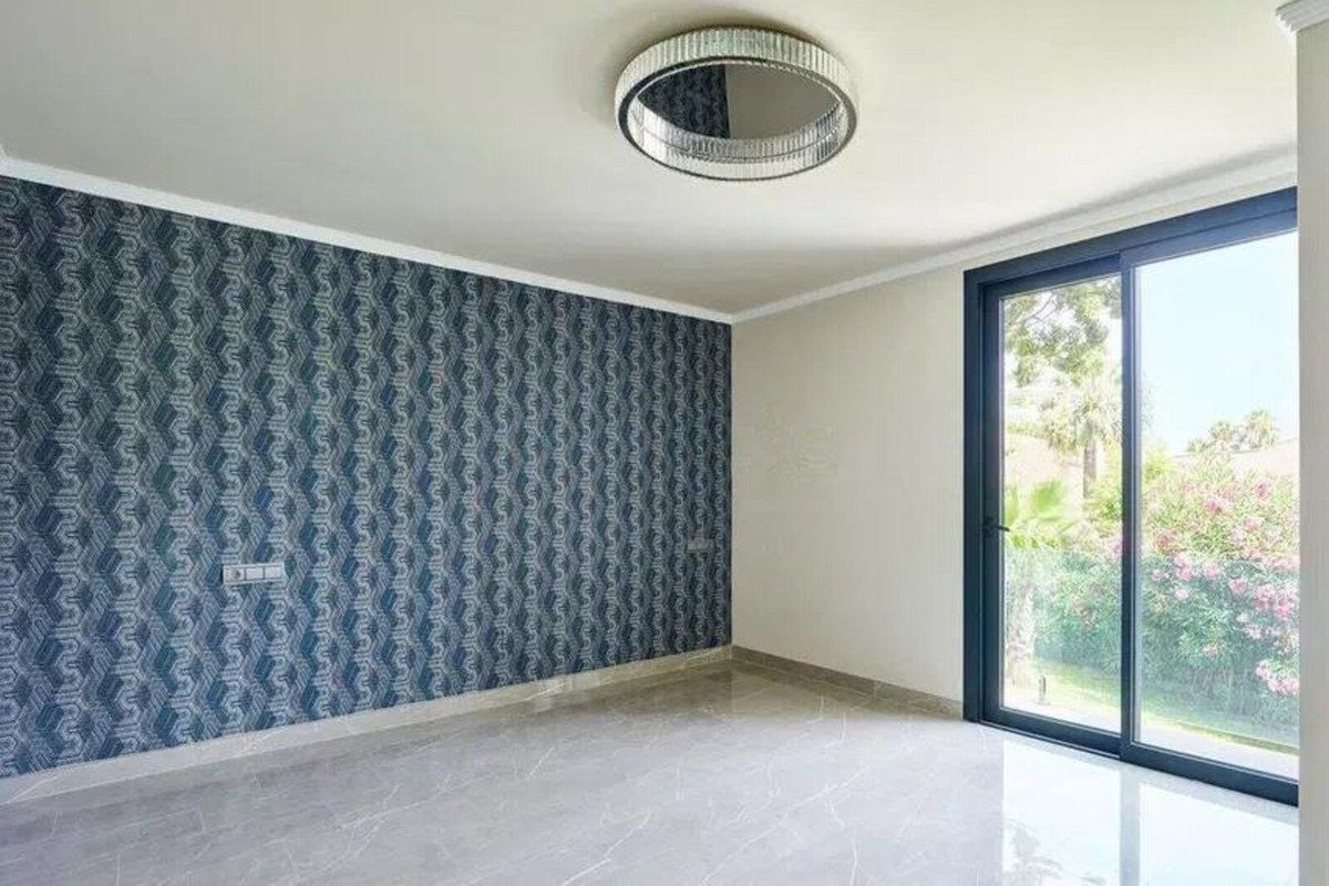 Empty room with patterned wallpaper and sliding glass doors opening to a lush garden view.