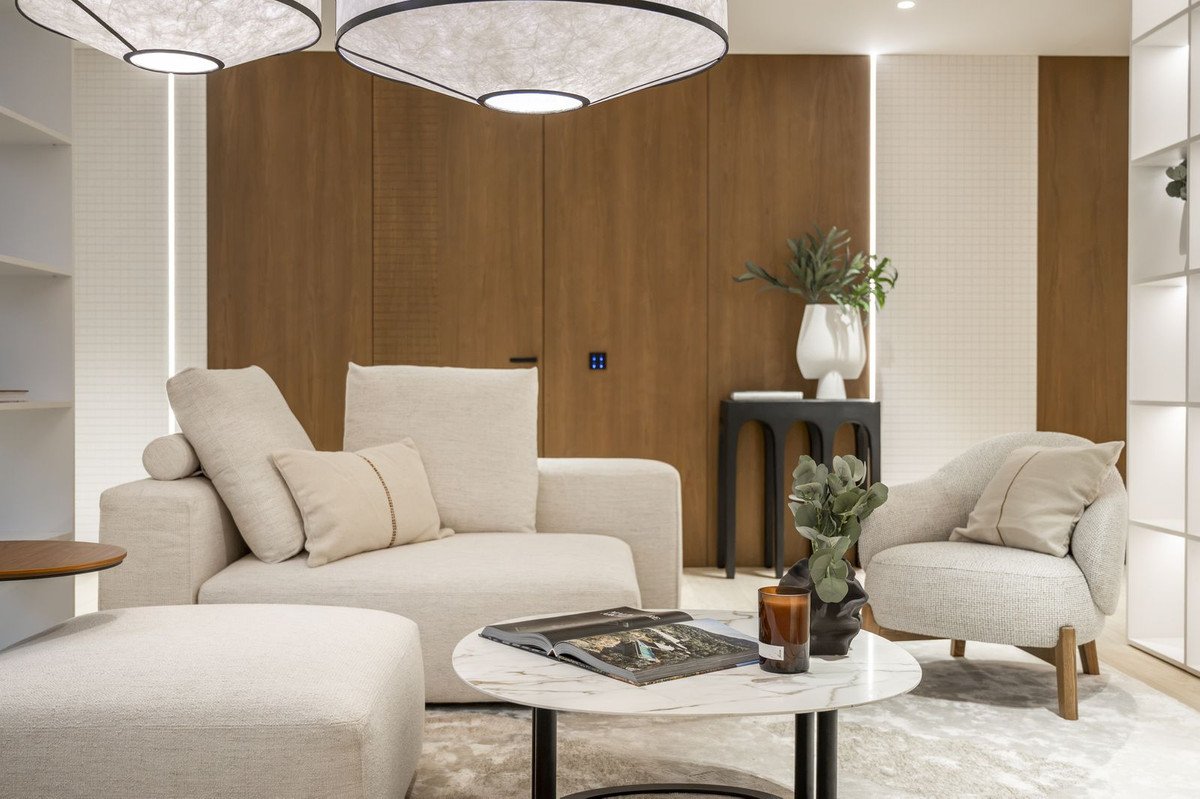 Modern living room with a beige sectional sofa, armchair, marble coffee table, and wooden accent wall.