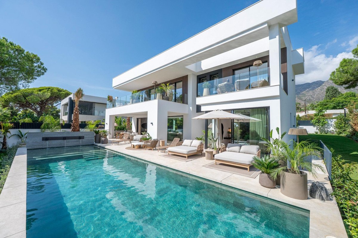 Modern villa with a swimming pool, sun loungers, and outdoor seating area with mountain views.