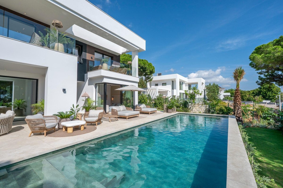 Modern white villa with a swimming pool, lounge chairs, and outdoor seating on a sunny day with blue sky.
