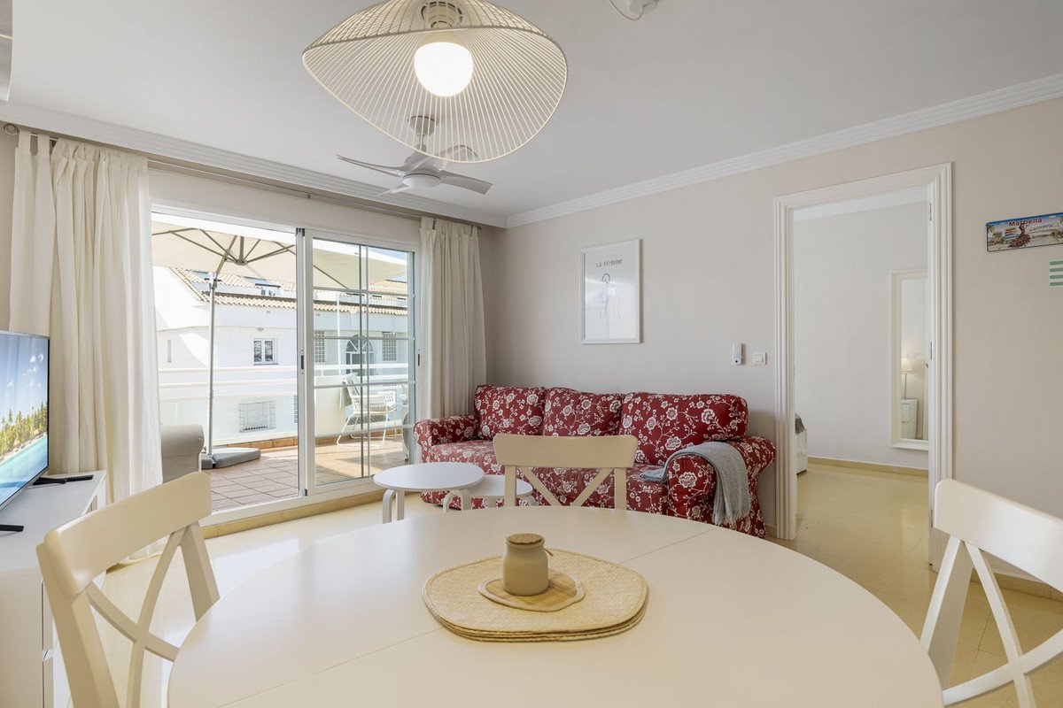 Modern living room with red floral sofa, dining table, and sliding doors opening to a terrace with an umbrella.