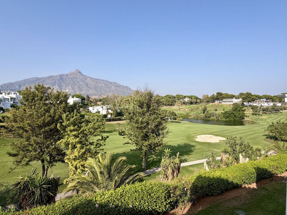 Balcony view of a lush golf course with a lake, sand trap, and a majestic mountain in the background under a clear blue sky.