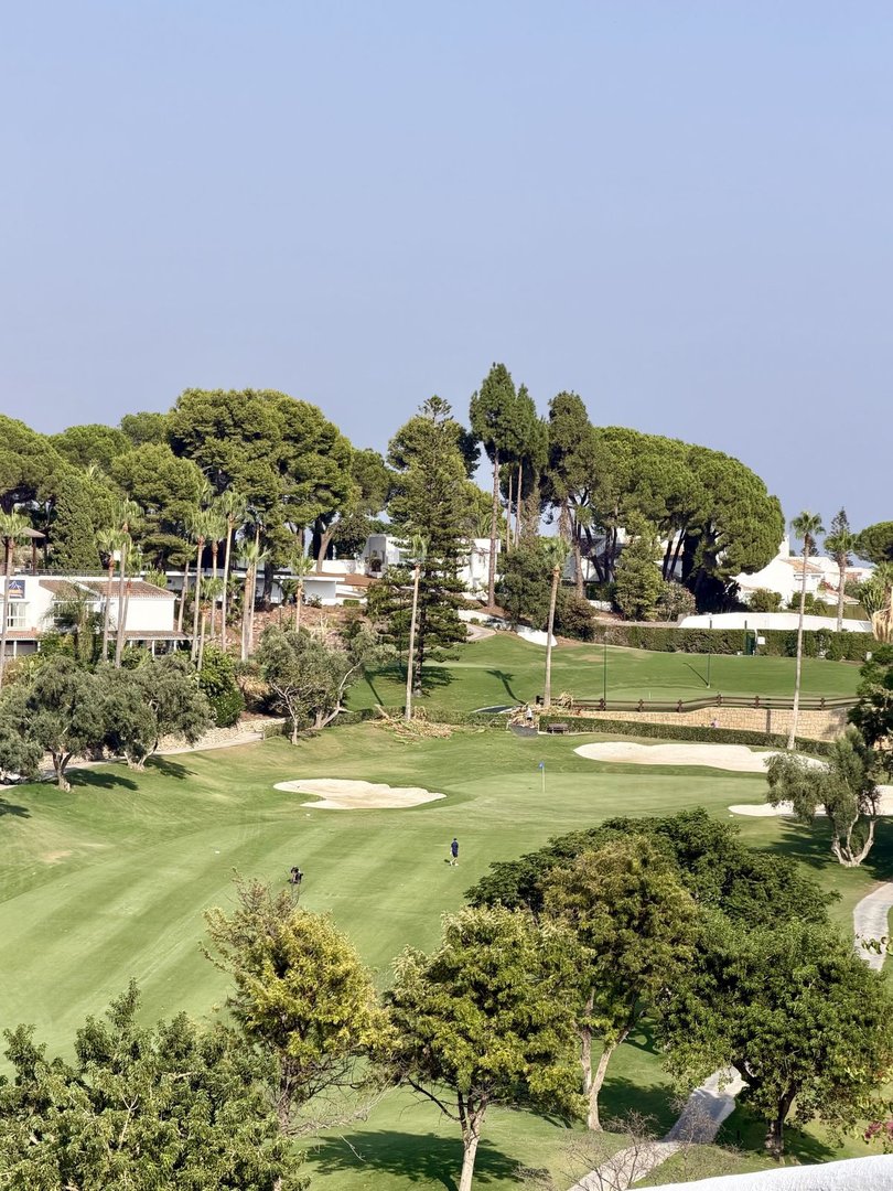 A scenic view of a lush green golf course with sand traps and trees, under a clear sky.