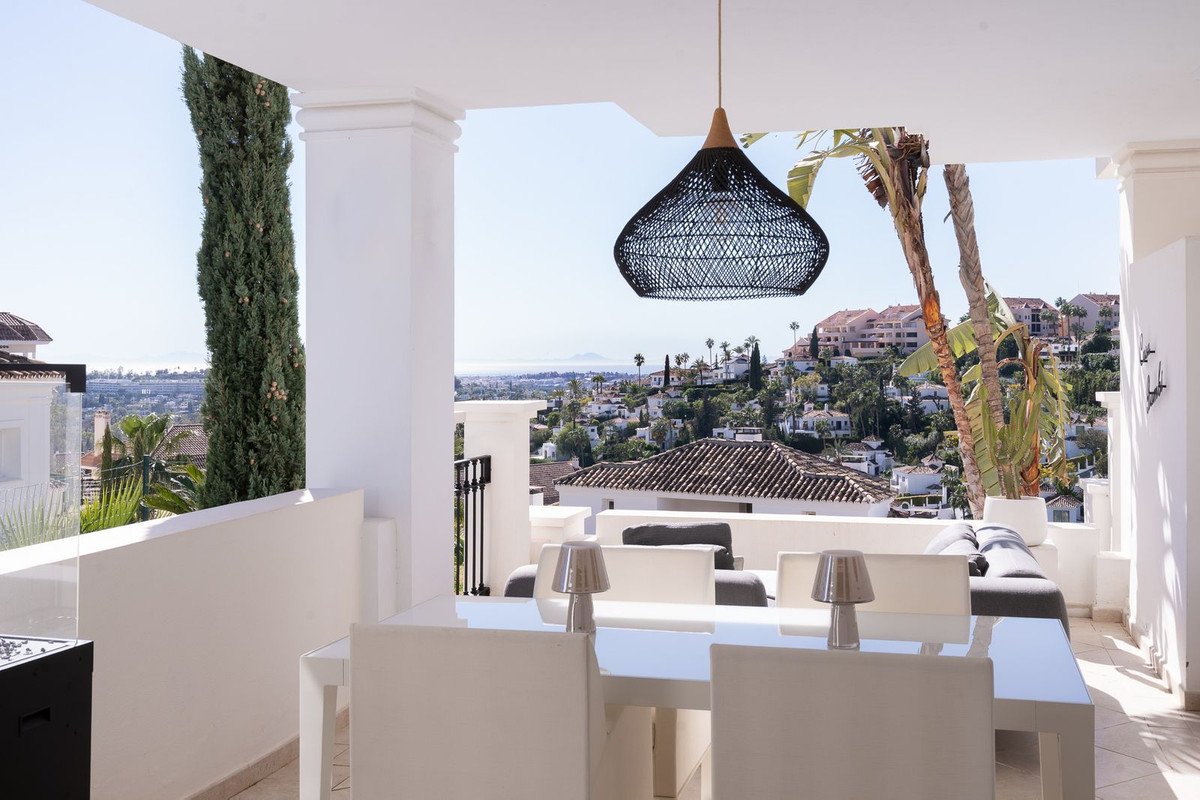 A bright terrace with a dining table and chairs, offering a panoramic view of the sea and surrounding hills.