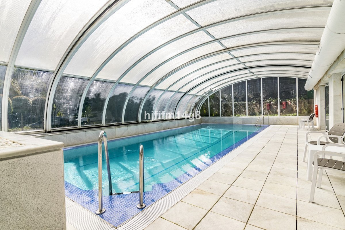 Indoor swimming pool with transparent arched roof and tiled deck
