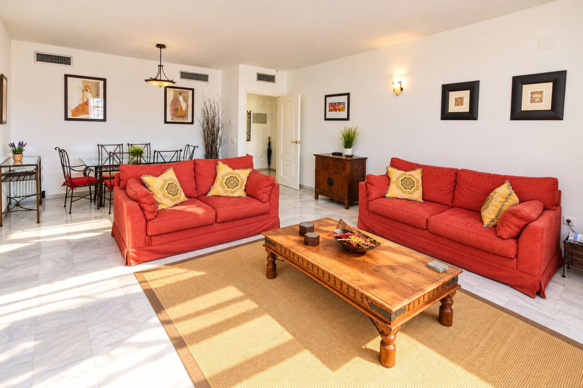 Bright living room with two red sofas, wooden coffee table, and dining area in background.