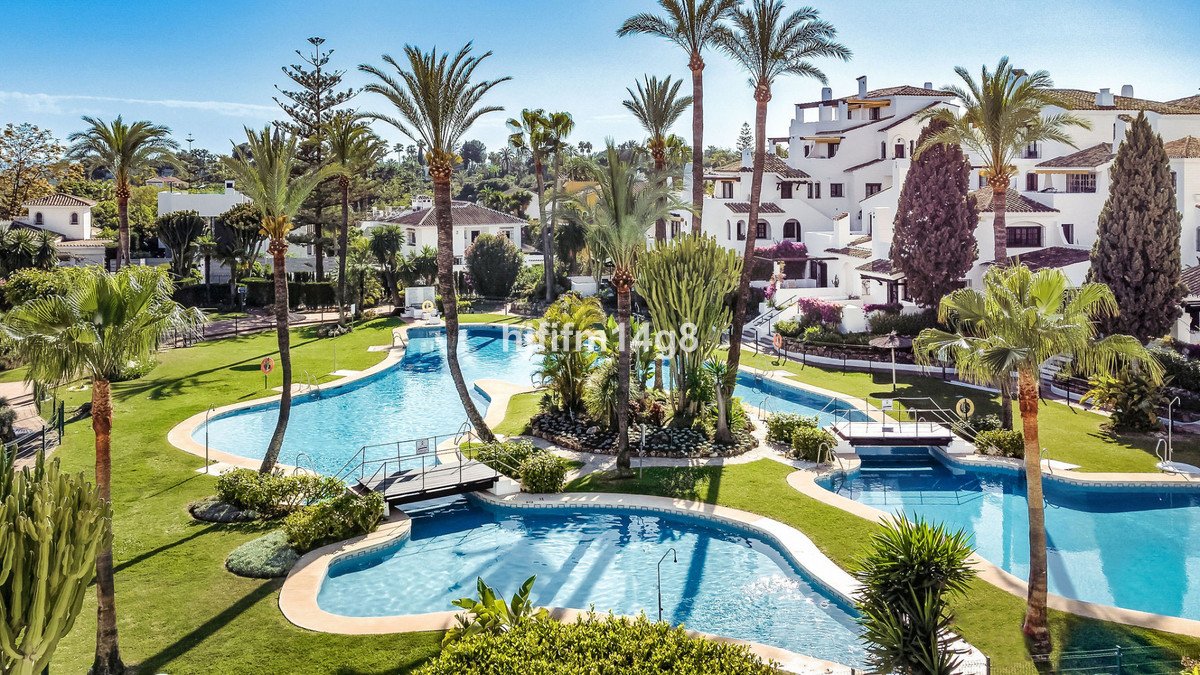 Resort pool area with palm trees and white buildings in background