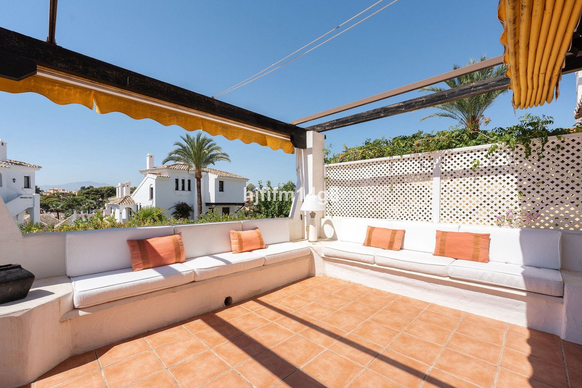 White terrace seating with orange cushions, overlooking palm trees and white houses
