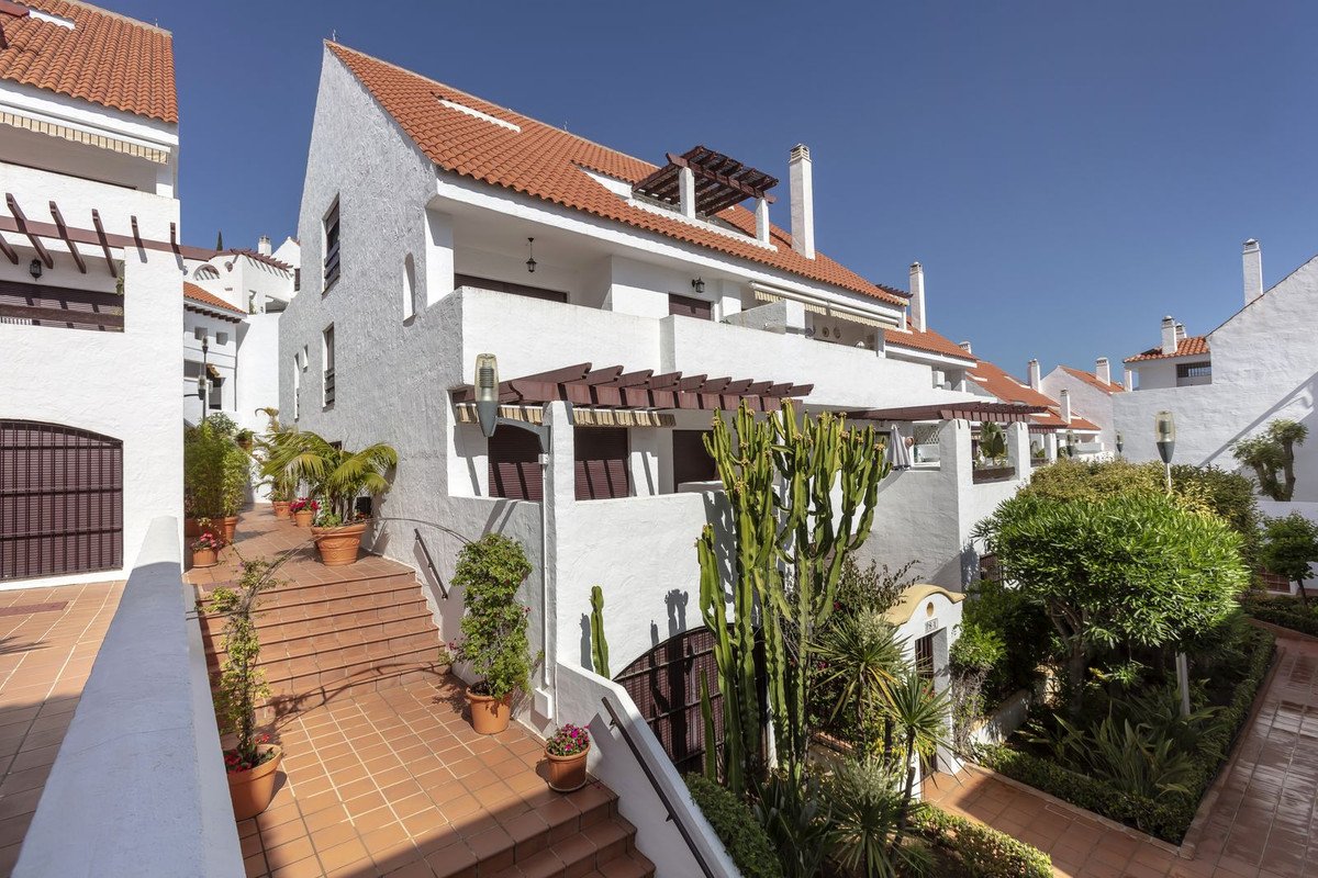 White apartment complex with terracotta roofs, terraces, and tropical garden.
