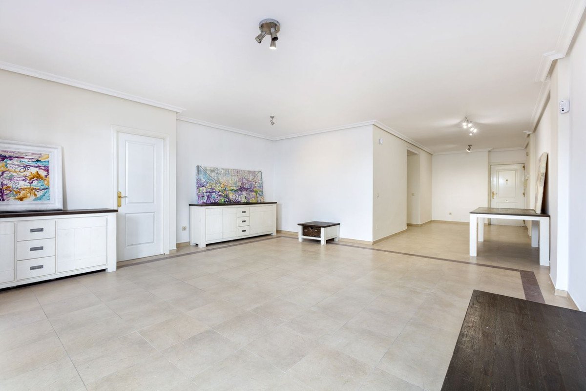 Spacious living room with white furniture, colorful artwork, and tiled flooring.