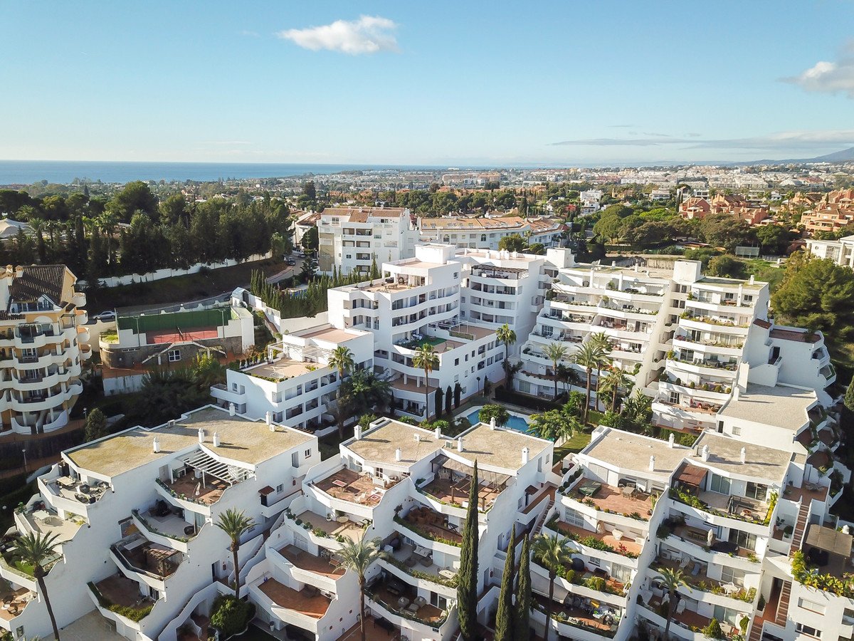 Aerial view of modern white resort apartments with terraces, overlooking the sea and distant hills.