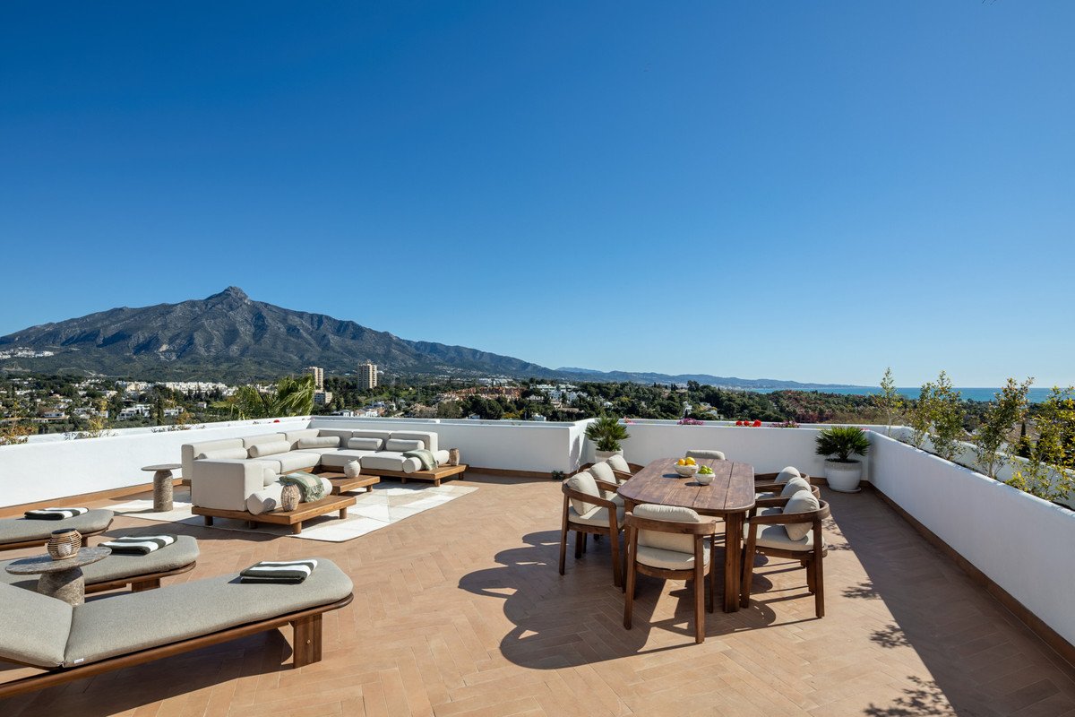 Spacious terrace with lounge seating and dining table offering panoramic mountain and sea views under a clear blue sky.