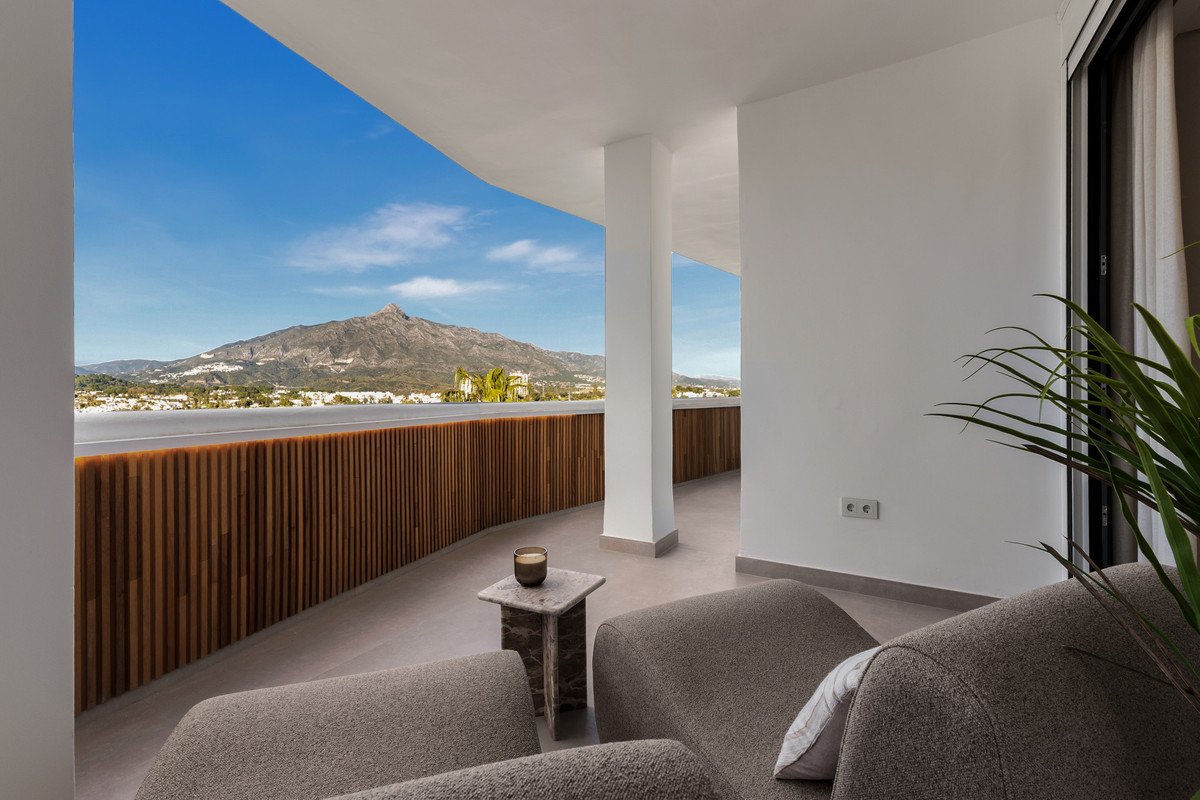 Modern balcony with comfortable seating and stunning mountain and coastal views under a clear blue sky.