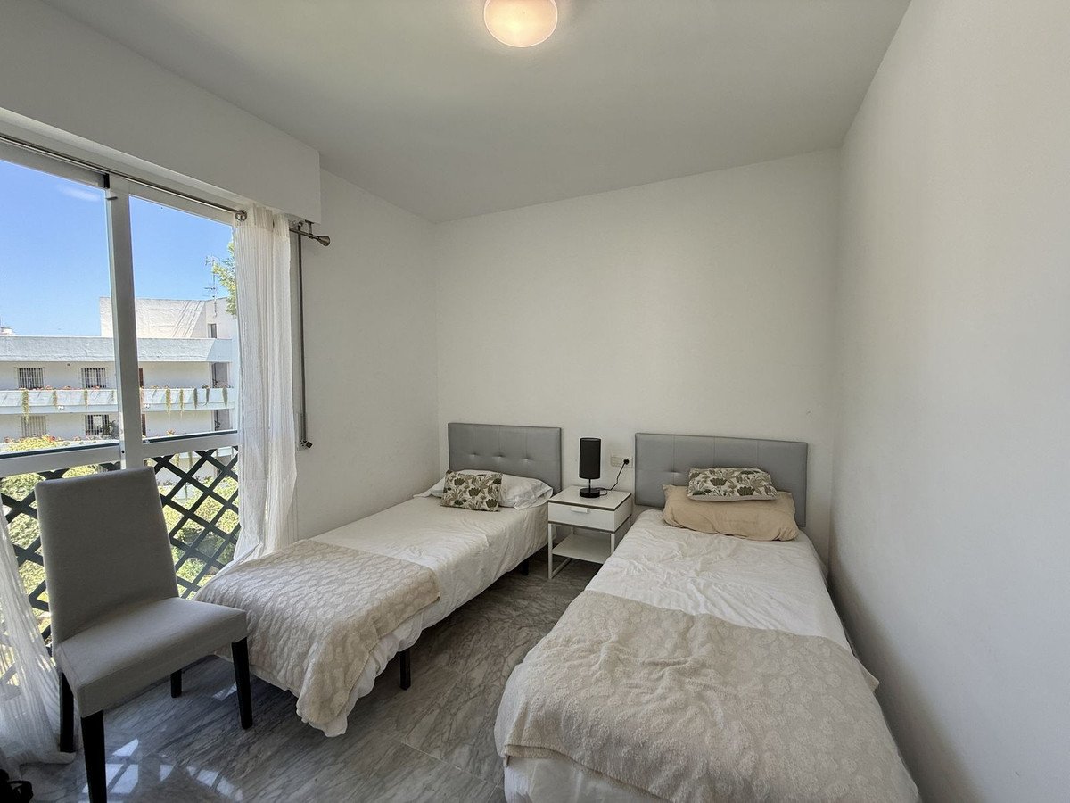 A bright twin bedroom with two single beds, a chair, and a balcony view.