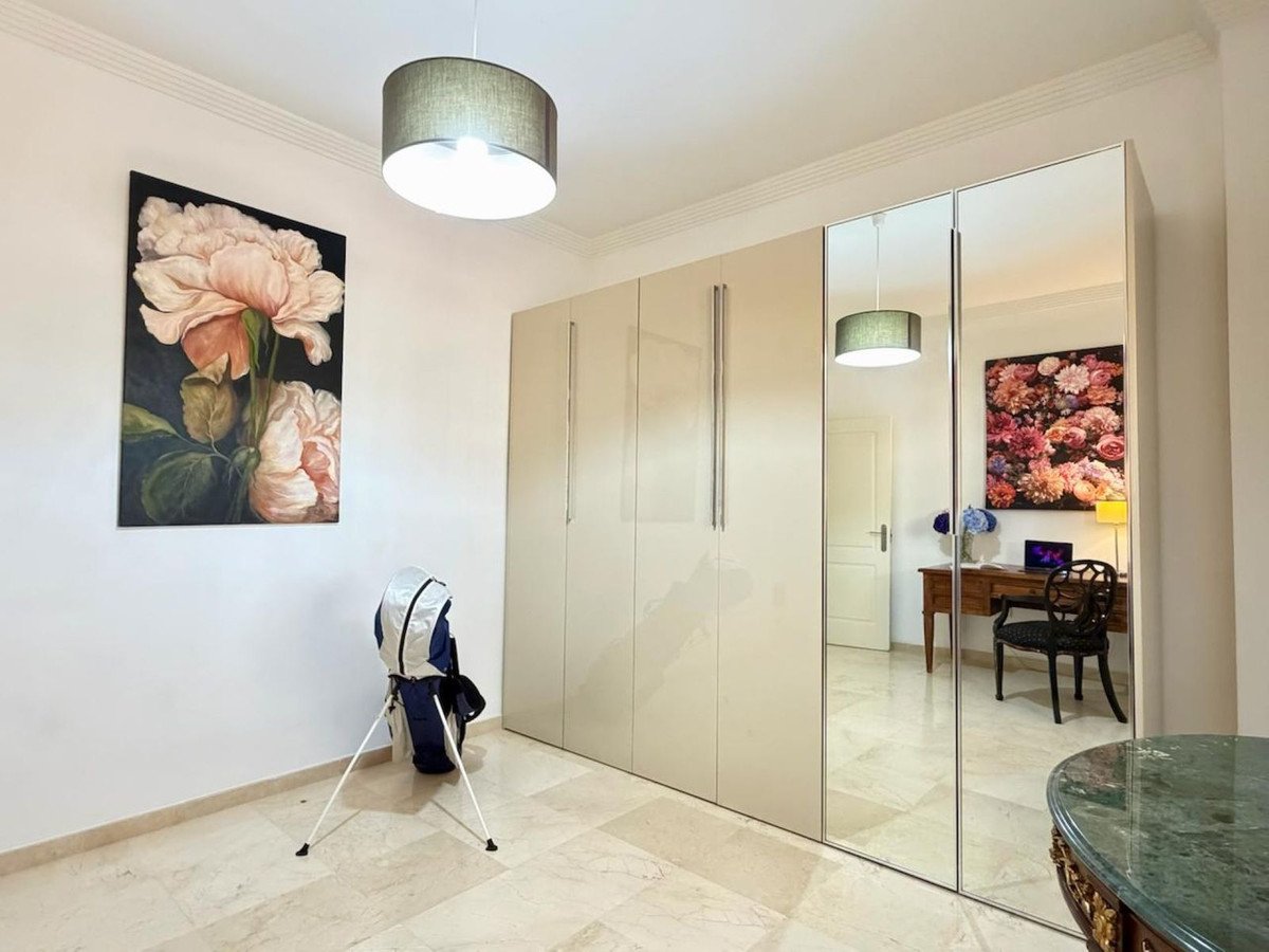 A bedroom with a large wardrobe featuring mirrored doors, artwork on the wall, and a desk with a chair reflected in the mirrors.