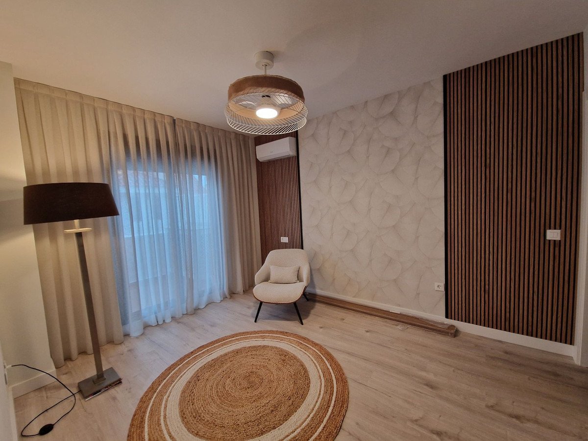 Modern living room with wooden accent wall, round rug, and large window curtains.