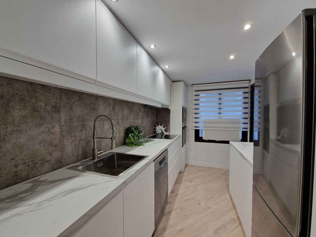 Modern kitchen with stainless steel appliances, marble countertops, and a window with blinds