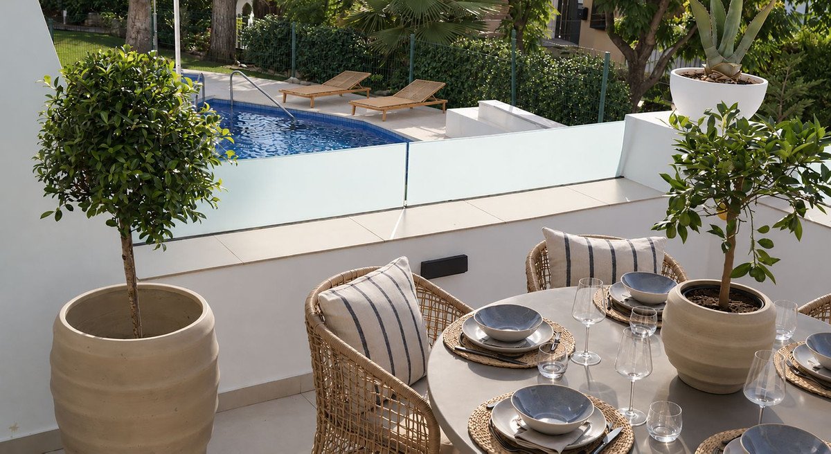 Outdoor dining area with pool view, potted plants, and wicker chairs