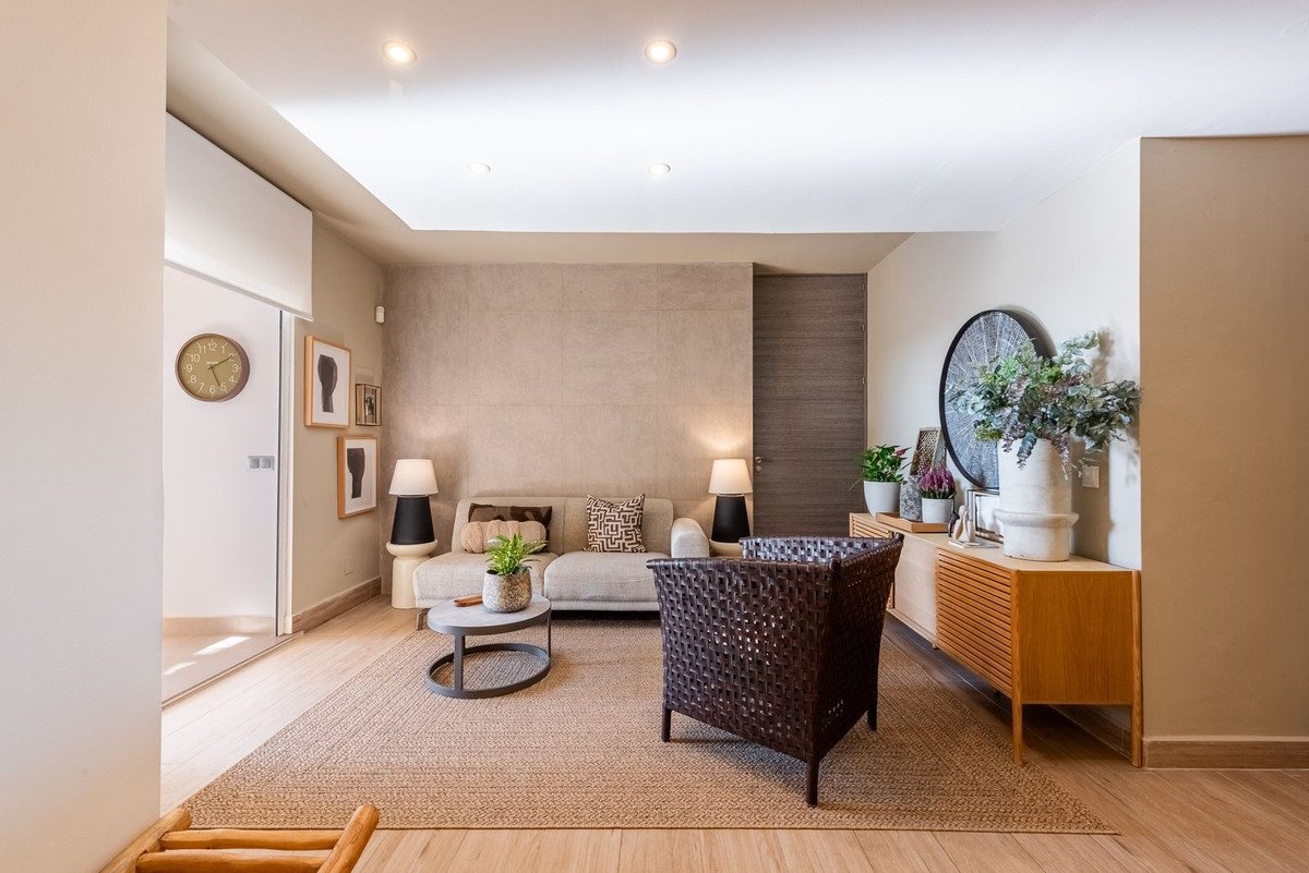 Modern living room with beige sofa, woven armchair, coffee table, and decorative items on a credenza.