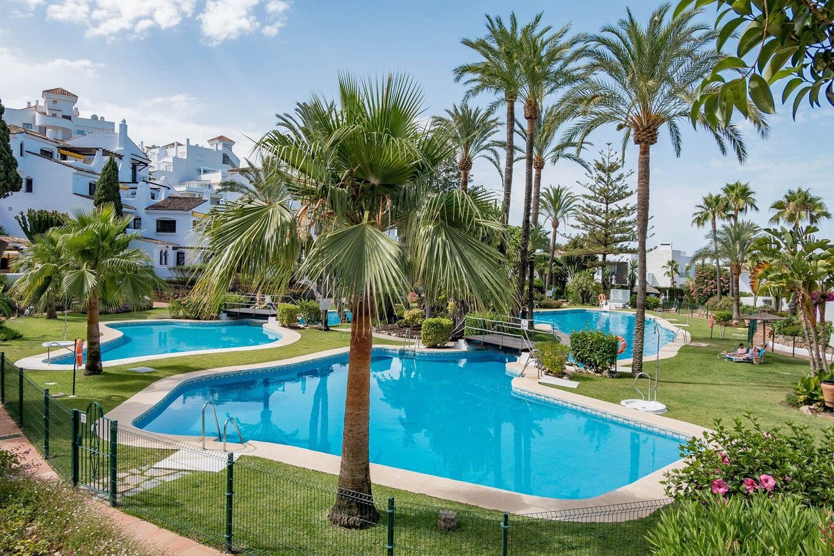 Resort swimming pool with palm trees and white buildings in background