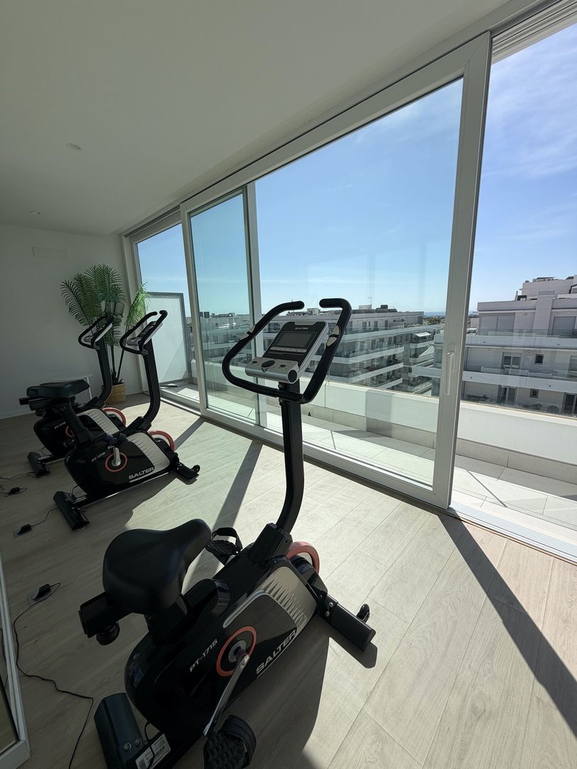Indoor gym with exercise bikes, large sliding glass doors, and a balcony with city views.