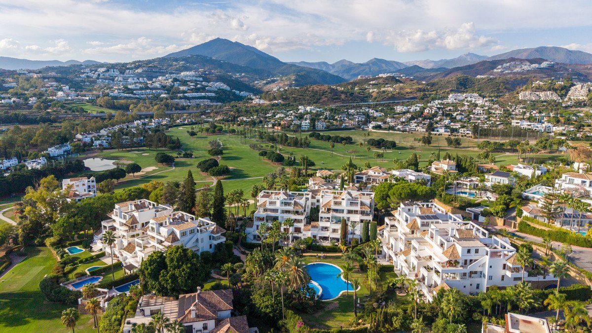 Aerial view of white apartment complex with swimming pool near golf course and mountains