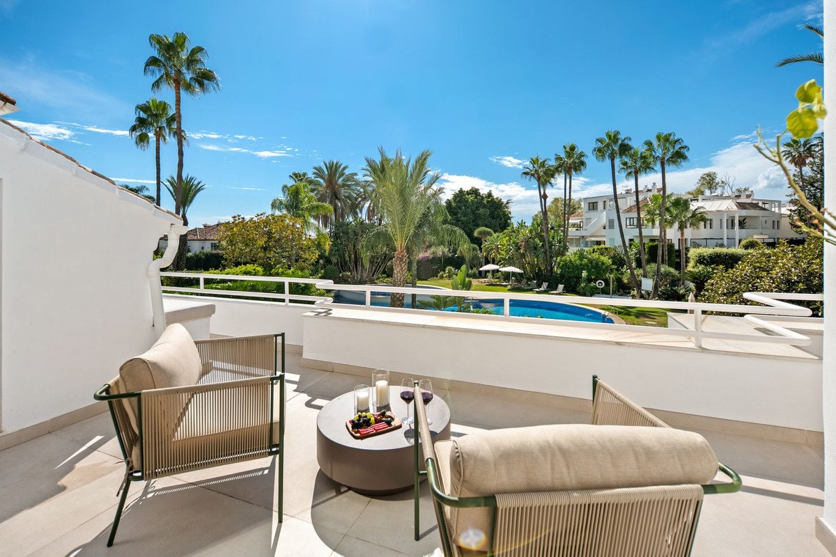 A balcony with outdoor seating overlooking a pool and palm trees.